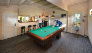 A garden room used as a games room with a pool table in the centre of the room.