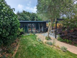 A garden room with grey cladding in a lush green garden.