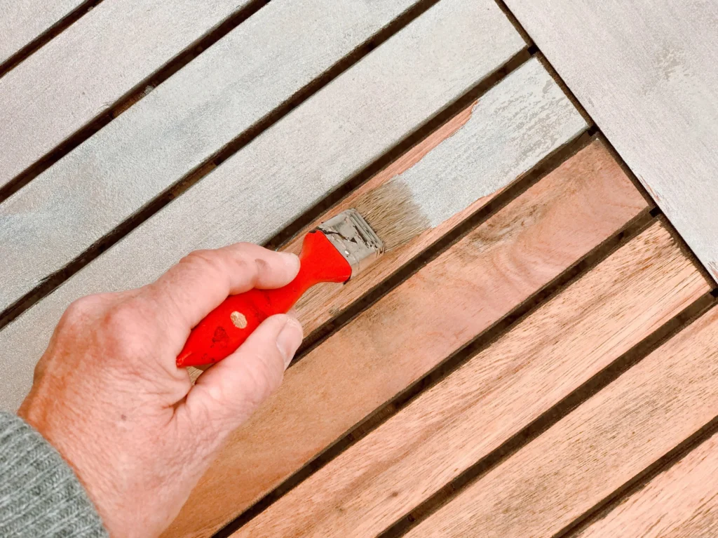 Brush applying pale grey paint to exterior timber boards.